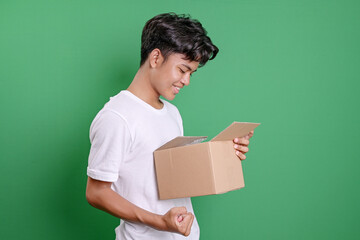 Young Asian Man Looking At Package With Happy Feeling Standing On Green Background