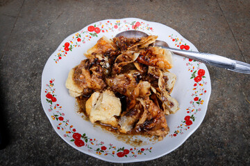 Close-up of Batagor, a traditional Indonesian street food from Bandung, served on a floral-patterned plate with peanut sauce and sweet soy sauce. A spoon rests beside the crispy fried dumplings