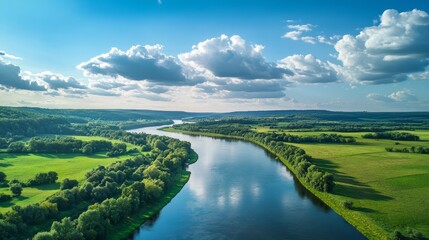 Obraz premium A serene river winding through lush green landscapes under a bright blue sky with clouds.