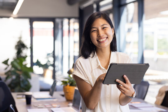 Smiling asian woman holding tablet in modern office, working on interior design project