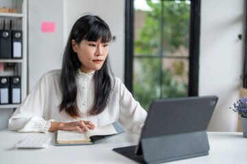 Asian businesswoman working using digital tablet and taking notes in office