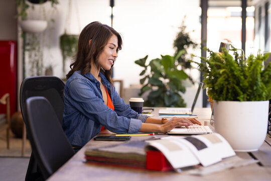At office, Working on computer, woman designing interior space with plants and coffee nearby