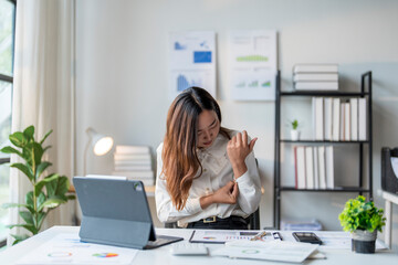 Asian businesswoman suffering from wrist pain while working on laptop computer at office