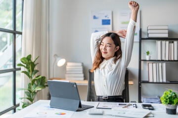 Young manager woman stretching her arms while working on tablet in office