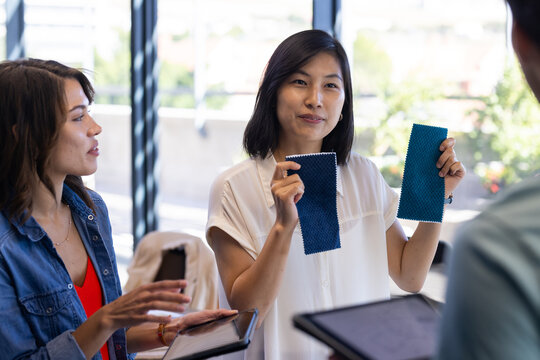 In office, diverse colleagues discussing fabric samples, holding swatches and using tablets - Powered by Adobe