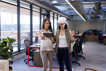 Using VR headset, asian woman exploring design while colleague holding tablet in office