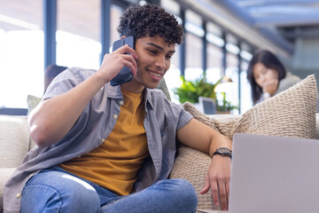 At office, Talking on smartphone, young man smiling and using laptop