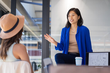 At office, Asian woman discussing project with client, showing room layout on tablet