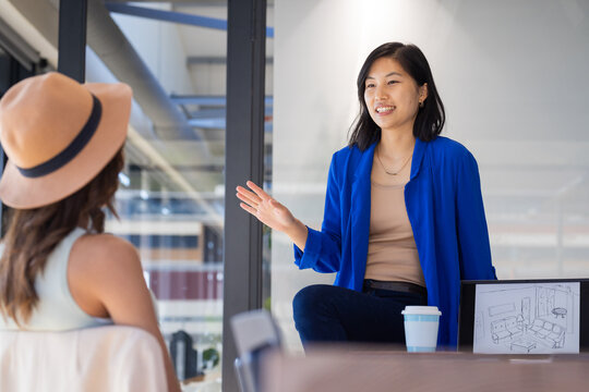 At office, Asian woman discussing project with client, showing room layout on tablet