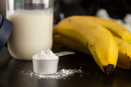 Creatine powder in a measuring scoop, pre-workout for gym and bananas on black wooden background.