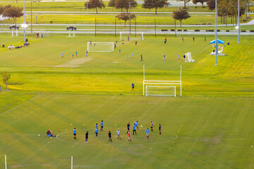 Aerial view of public sports park with children engaged in football game on grass stadium at sunset. Active way of life concept