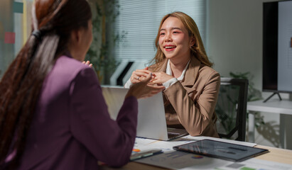 Two businesswomen are sitting at a table in a conference room, talking, discussing, meeting, financial business information. Online marketing, information, documents, laptop in modern office.