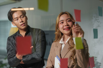 A team of business men and women wrote and pointed at sticky notes on the glass to brainstorm...