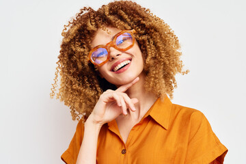 Cheerful woman with curly hair wearing orange glasses and a bright orange shirt, posing against a...