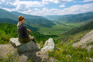  woman tourist is sitting on top of a mountain and enjoying the view of mountains in summer. concept of freedom, feelings of peace and happiness