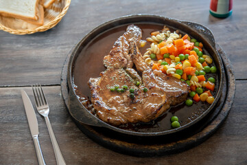 Serve t-bone pork stake on hot pan on wood table