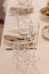 A table with a white tablecloth and a set of wine glasses and knives. The wine glasses are arranged in a row, with the tallest one in the middle and the shortest one on the left