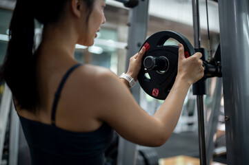 Fototapeta premium A sporty Asian woman placing a plate weight on a machine during her workout at the gym.