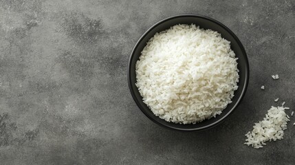 Minimalist image of white rice in a black bowl, top view on a grey background, emphasizing clean design and presentation.