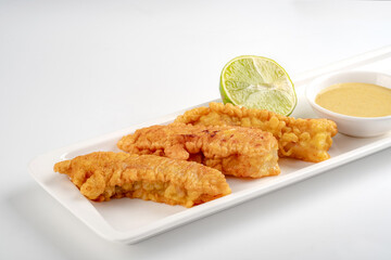 Fish fillets fried in breadcrumbs and served in a white plate on a white background. Fish sticks dish with sauce and lime
