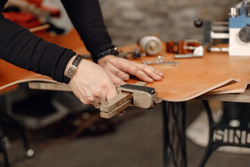 Cropped photo of a leather craftsman hands working on a belt