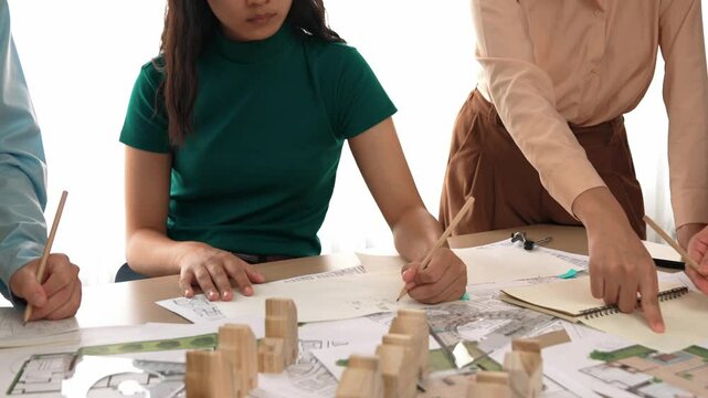 Smart architect and safety engineer discussion about building blueprint on table with architectural document, measurement tools and wooden block scatter around at modern office. Closeup. Delineation.
