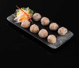 A beautifully plated dish of Asian meatballs on a black rectangular plate, garnished with fresh...