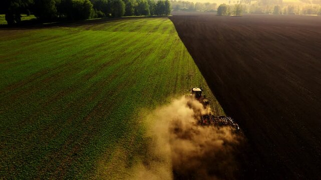 Tractor working the fields at sunrise in a rural landscape with dust clouds rising