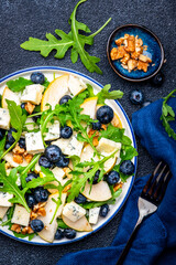 Tasty salad with pears, blueberries, roquefort cheese, arugula and nuts. Black background, top view