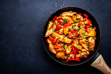 Stir fryed chicken slices with pineapple, paprika, chives, garlic, ginger, soy sauce and sesame seeds. Black background, top view