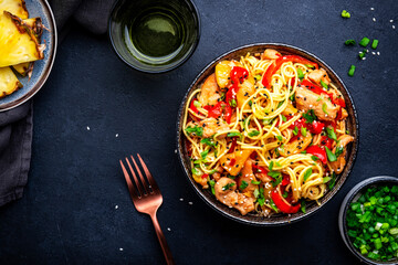 Stir fryed noodles with chicken slices, pineapple, red paprika, onion, soy sauce, garlic, ginger and sesame seedsl. Black background, top view