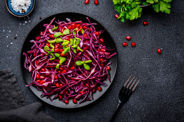 Vegan raw red cabbage salad with pomegranate seeds and sunflower sprouts on black background. Top view