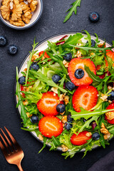 Vegan strawberry and herbs salad with arugula, blueberries and walnuts on black background. Top view