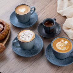 A cozy coffee setup with four cups of various coffee drinks and a pastry on a wooden table.