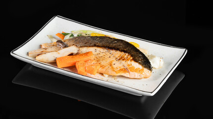 A delicious and fresh grilled salmon fillet served with vegetables on a white rectangular plate against a black background.