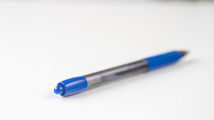 A blue pen with a black tip sits on a white surface. The pen is not in use and is laying on its side. Concept of simplicity and minimalism