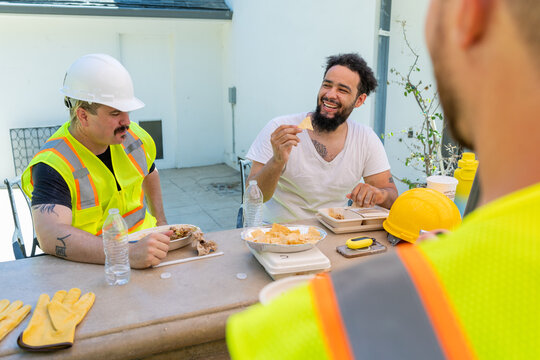 During a break in the middle of a house remodeling project, two construction workers wearing safety vests and helmets take a moment to enjoy a lighthearted conversation, showcasing their camaraderie