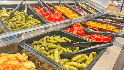 A salad bar with many different types of vegetables, including pickles. The vegetables are arranged in several bowls, and there are several spoons for picking up the food