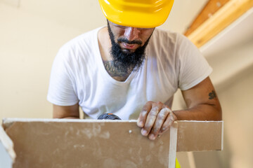 A focused construction worker in a safety helmet skillfully installs drywall as part of a detailed home renovation project that demands significant skill and precision for excellent results