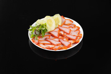 A plate of beautifully arranged sliced pork with fresh vegetables and lemon slices, set on a sleek black background.