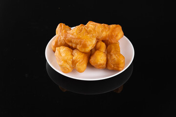 A plate of golden brown deep-fried dough sticks on a white dish against a black background, appetizing and delicious snack.