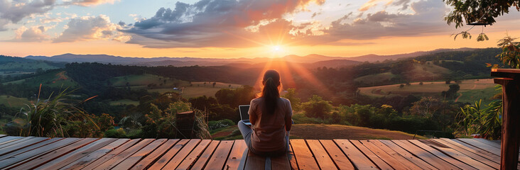 young freelancer woman working at the computer at sunset or sunrise on the top of the mountain