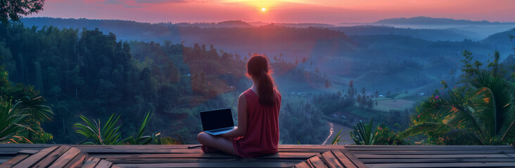 young freelancer woman working at the computer at sunset or sunrise on the top of the mountain
