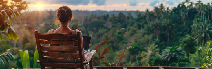 young freelancer woman working at the computer at sunset or sunrise on the top of the mountain