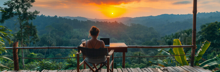 young freelancer woman working at the computer at sunset or sunrise on the top of the mountain