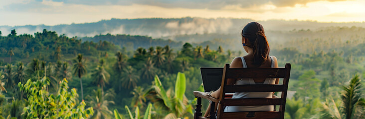 young freelancer woman working at the computer at sunset or sunrise on the top of the mountain