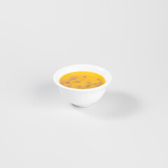 A small bowl of soup with visible ingredients like herbs and pieces of meat, placed on a plain white background.
