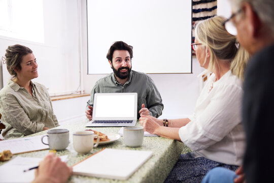 Smiling businessman showing laptop with blank screen to colleagues during meeting in office