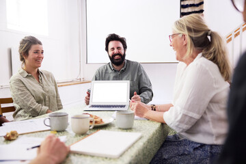 Cheerful businessman showing laptop with blank screen to colleagues during meeting in office