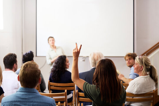 Businesswoman with hand raised sitting behind colleagues during meeting in office